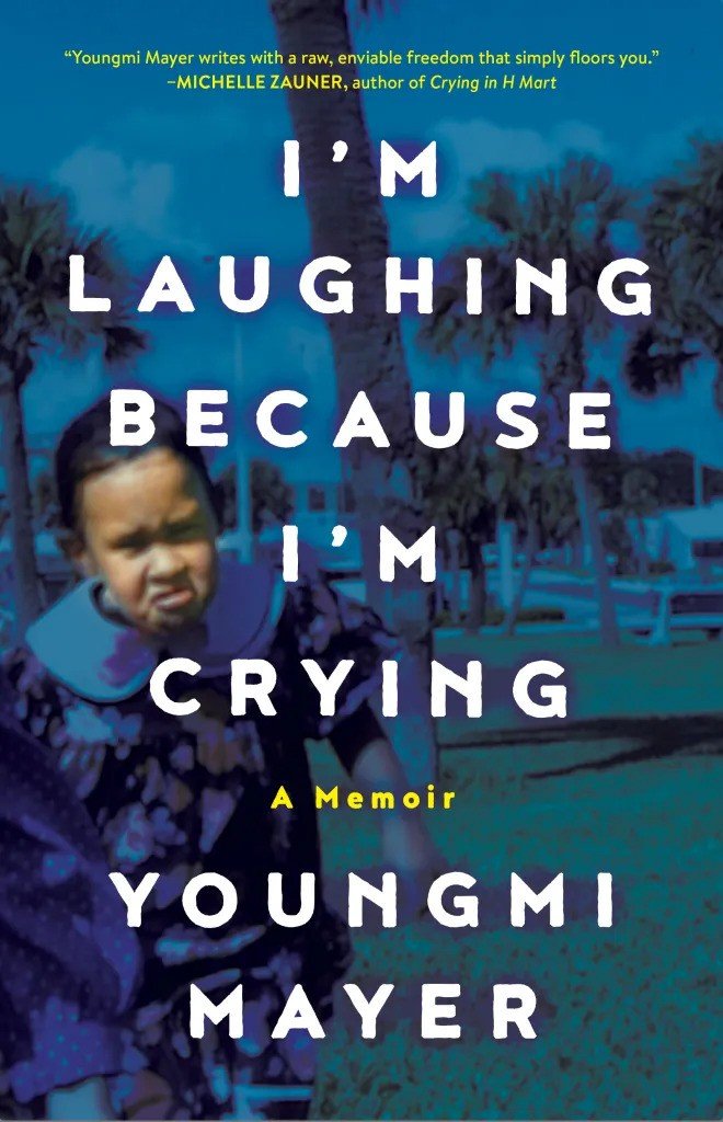 Signed & personalized copy of Im Laughing Because Im Crying: A Memoir by Youngmi Mayer from Yu & Me Books. The cover shows a blurred photo of a young girl with trees and blue sky, overlaid with bold white and yellow text.