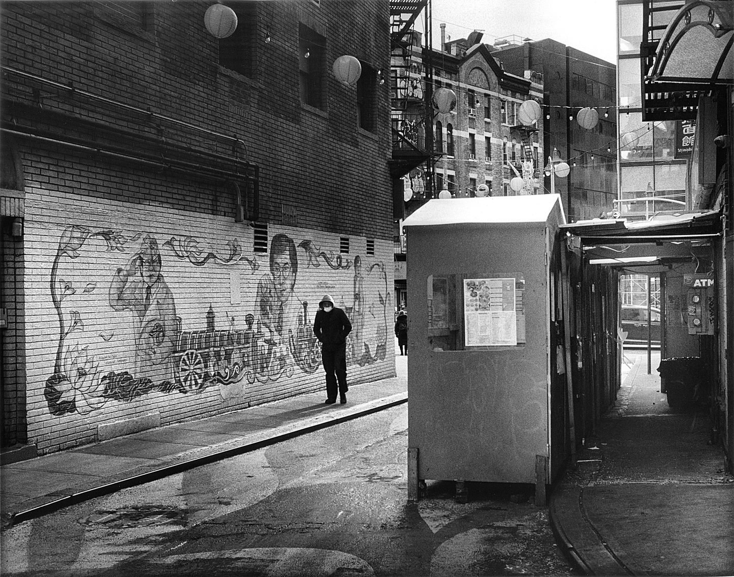 A person walks through a narrow Manhattan Chinatown alley as seen in "Tiny Grains" by Edward Cheng (Signed!), available at Yu & Me Books. Brick buildings, animal murals, paper lanterns, a booth, and ATM create classic Chinatown photography vibes.