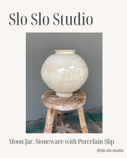 A large, round moon jar with a narrow opening sits on a rustic wooden stool. Cream-colored and crafted from stoneware with porcelain slip, the jar is set against a gray wall. Its understated elegance recalls the inviting charm of creative community spaces like those found at Yu & Me Books in NYC. Text reads: [Raffle] Support Village Works Bookstore! by Yu & Me Books.