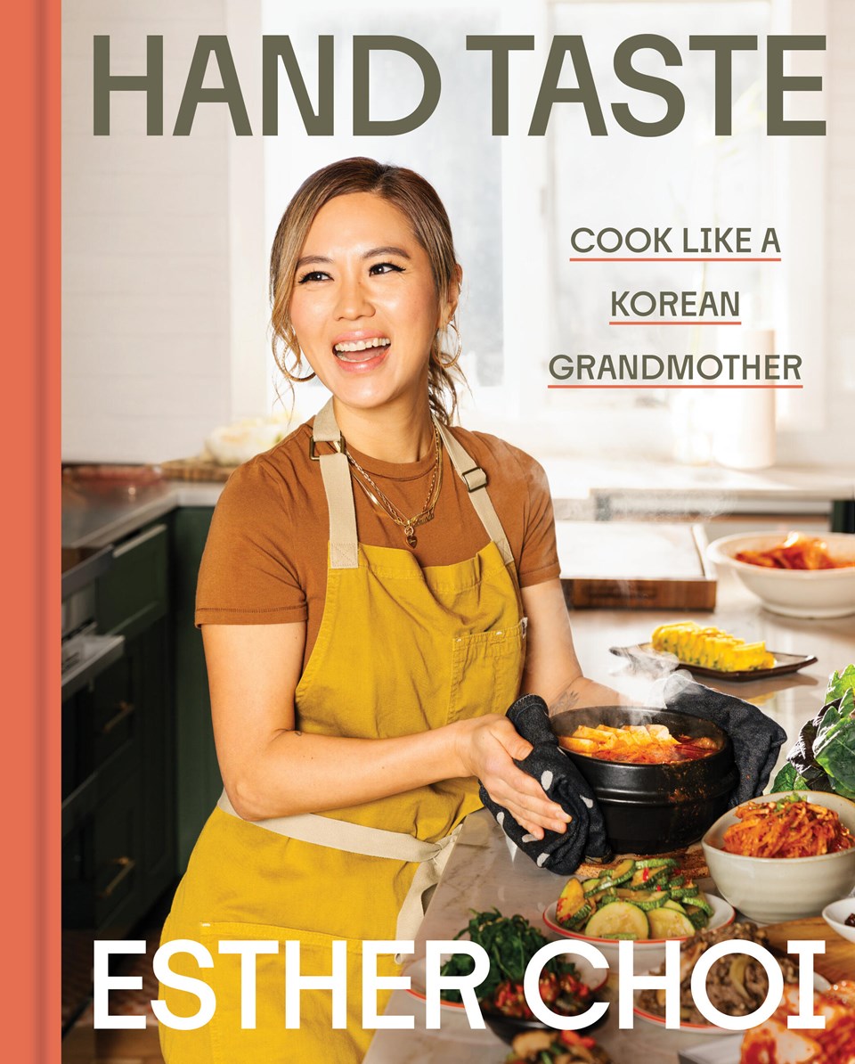 A smiling woman in a yellow apron holds a hot dish in a kitchen, with the text “[Korea Society Event] Hand Taste by Esther Choi” and “Yu & Me Books” overlaid—offering an inviting glimpse into this cherished Korean cookbook by Esther Choi.