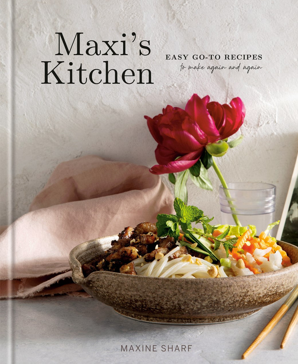 The cover of Maxi’s Kitchen by Maxine Sharf (Signed! Limited Qty), available from Yu & Me Books, displays a bowl with noodles, vegetables, and meat, a pink napkin, red peony, and water glass—welcoming you to easy, tasty recipes.