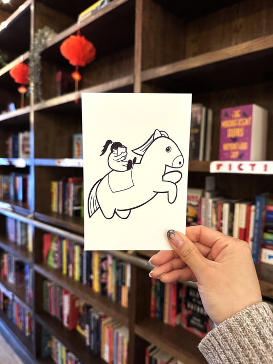 A hand holds the "Year of the (Chonky) Horse, Yu & Me Postcard" from Yu & Me Books, featuring an illustrated girl riding a chonk horse, set against shelves of colorful books and red lanterns.
