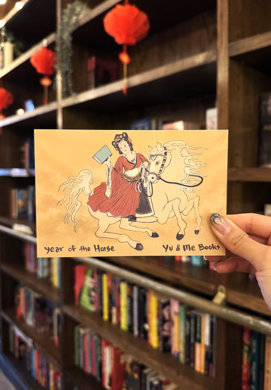 A hand holds the Year of the Horse, Yu & Me Postcard (Limited Release!) from Yu & Me Books, featuring a woman in a red dress on a white horse with bookshelves and red lanterns in the background.